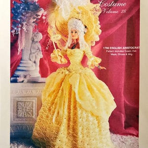 May include: A doll in a yellow crochet gown, hat, and wig, reminiscent of an 18th-century English aristocrat. The image is from a "Crochet Collector Costume" pattern book, volume 28. The pattern includes the gown, hat, mask, shoes, and wig.