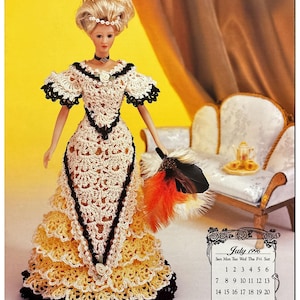 Puede incluir: Una muñeca de ganchillo con un vestido blanco y amarillo con ribetes negros. La muñeca sostiene un abanico de plumas. La muñeca está sentada en un sofá blanco con un fondo amarillo. La imagen también incluye un calendario para julio de 1996.
