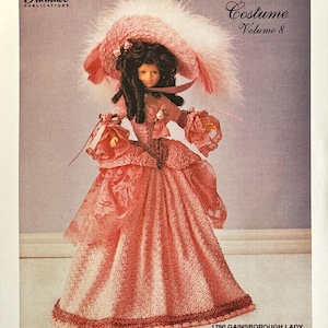May include: A doll in a pink Gainsborough-style dress, hat, and bloomers, with a matching purse. The doll has dark hair and is featured on the cover of a "Crochet Collector Costume" pattern book, volume 8, from Paradise Publications.