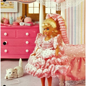 May include: A Barbie doll wearing a pink and white ruffled crochet dress, standing in a dollhouse bedroom. The doll has blonde hair and is wearing pink shoes. The image includes the text "Ruffled Dress".