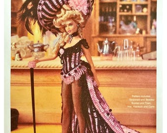 May include: A doll in a crochet costume from the "Crochet Collector Costume Volume 87" pattern. The doll wears a black and pink bustier, a long train, and a large hat with feathers and a pink flower. The image includes the text "1899 WILD WEST SHOWGIRL".