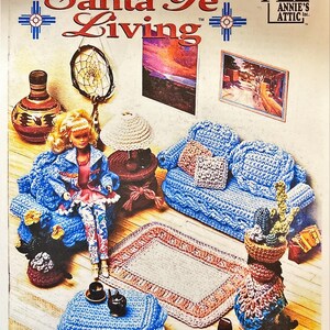 May include: A doll sitting on a blue crocheted sofa, part of a Santa Fe Living collection. The image features a crocheted rug, table, and other decorative items. The cover art includes the text "Santa Fe Living" and "Annie's Attic".