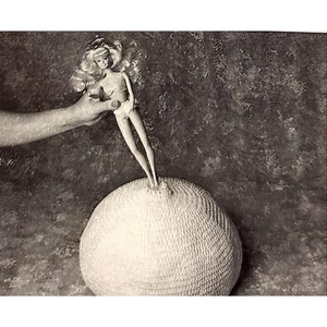 May include: A white crocheted ball with a doll standing on top of it. The doll is wearing a white swimsuit and has blonde hair.