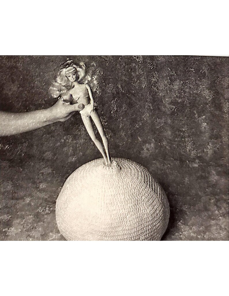 May include: A white crocheted ball with a doll standing on top of it. The doll is wearing a white swimsuit and has blonde hair.