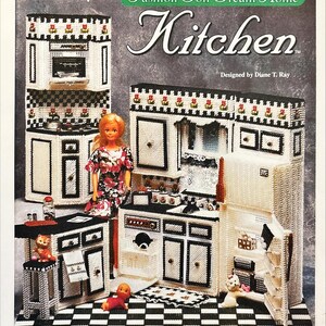 Op de afbeelding: Een plastic canvas patroon voor een poppenkeuken. Het ontwerp omvat een fornuis, kasten en een koelkast, allemaal in zwart en wit. De tekst luidt "Fashion Doll Dream Home Kitchen" en "Designed by Diane T. Ray."