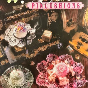 May include: A craft book cover titled Annie's Attic Antique Crochet Pincushions featuring a black sewing machine, a small wooden box, and three crocheted pincushions in white, sage green, and pink with floral accents and pins.