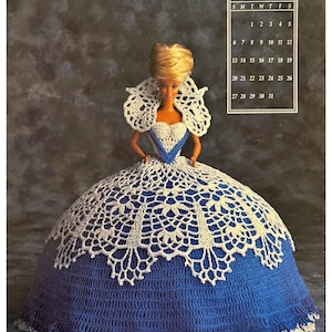 May include: A crochet doll dress in blue and white. The dress has a white lace overlay and a blue crochet base. The dress is designed for a doll with a waist measurement of approximately 25 cm. The dress is shown on a doll with blonde hair and a blue dress.