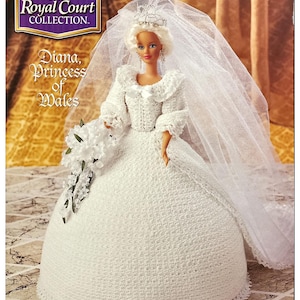 May include: A crochet doll dressed in a white wedding gown with a veil and tiara. The doll is holding a bouquet of white flowers. The doll is part of The Royal Court Collection and is named Diana, Princess of Wales.