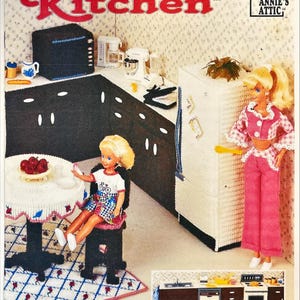 May include: A plastic canvas pattern for a Fashion Doll Kitchen, featuring a miniature kitchen scene with a doll, appliances, and furniture. The scene includes a doll in a pink outfit, a table, and a refrigerator.