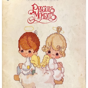 May include: A cross-stitch pattern book titled "Precious Moments" featuring two cherubic figures with halos and wings. The cover includes the text "Gloria and Pat Present" and the price $4.00.