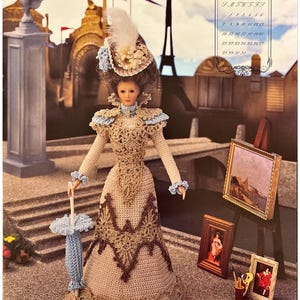 May include: A crocheted doll wearing a brown and beige dress with a blue and white hat and holding a blue umbrella. The doll is standing in front of a painting on an easel and a calendar with the month of May.
