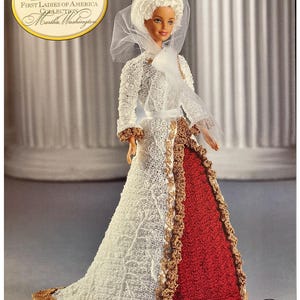 Puede incluir: Muñeca Barbie de la colección First Ladies of America, edición Martha Washington. La muñeca viste un vestido blanco de ganchillo con un panel de falda rojo, adornado con detalles dorados. Un gorro y velo blancos completan el conjunto histórico.