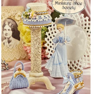 May include: A display of miniature crochet items, including a hat, purse, and shoe, on a pink satin surface. The hat is on a decorative stand. A figurine in a blue dress holds a parasol. The image includes text that reads "Annie's Miniature Shoe Society."
