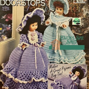 Könnte beinhalten: Zwei gehäkelte Puppen-Türstopper, einer in hellblau und einer in lila, mit weißer Spitzenborte. Die Puppen tragen Hüte und Kleider. Der Text "Makes A Great Pajama Bag Too!" ist auf dem Bild gedruckt.