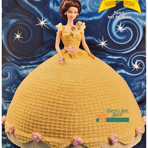 Puede incluir: Una muñeca de crochet vestida como Bella de La Bella y la Bestia. La muñeca lleva un vestido amarillo con una rosa rosa y una corona. La muñeca está de pie sobre un fondo azul con estrellas. El texto "The Fairy Tale Collection" y "Beauty and the Beast" está en la parte superior de la imagen. El texto "Faith's She Shed" está en la parte inferior de la imagen.