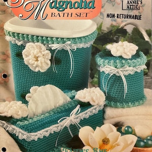May include: A crochet bathroom set with a teal and white color scheme. The set includes a tissue box cover, a wastebasket, and two containers with lids. The containers have white flowers on the top. The set is labeled "Sweet Magnolia Bath Set" and "Annie's Attic".