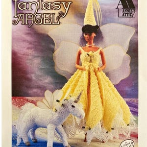 Puede incluir: Un patrón de ganchillo para una muñeca Fantasy Angel con un vestido amarillo, alas y un unicornio a juego. La imagen presenta el texto "CROCHET Fantasy ANGEL" y el logotipo de Annie's Attic. La muñeca lleva un vestido amarillo de ganchillo.