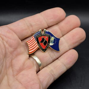 May include: A gold-colored pin with a red, white, and blue American flag and a blue, white, and gold Air Force flag. The pin features a red shield with a black silhouette of a dog and the words "Military Working Dog, Guardians of the Night".