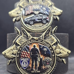 May include: Two circular brass-toned commemorative coins featuring relief-sculpted German Shepherd heads. The front coin displays a police officer with a K9, the US flag, the South Carolina flag, a police badge, and text: OFFICER DON DJ KELLER GREENWOOD POLICE DEPARTMENT EOW MAY 11 2026.