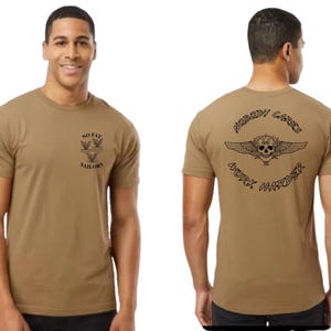 May include: A tan crew neck t-shirt with black graphics. The front of the shirt has the text "NO FAT SAILORS" with a graphic of three birds. The back of the shirt has the text "NOBODY CARES WORK HARDER" with a skull and wings graphic.