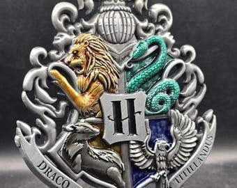 May include: A silver-colored emblem featuring a lion, snake, badger, and eagle, with the letter "H" in the center. The emblem has the words "DRACO" and "TITILLANDUS" on it, and the words "DORMENS NUNQUAM" are at the bottom.