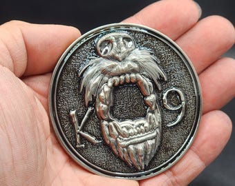 May include: A silver-toned metal belt buckle with a detailed design of a snarling creature with a long beard. The buckle is circular and has the letters "K9" on the side.