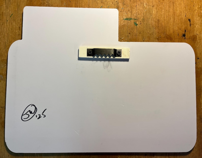 May include: A white rectangular sign with rounded corners and a small rectangular extension at the top. A metal sawtooth hanger is attached to the back. The artist's signature and the number 125 are in the lower left corner.