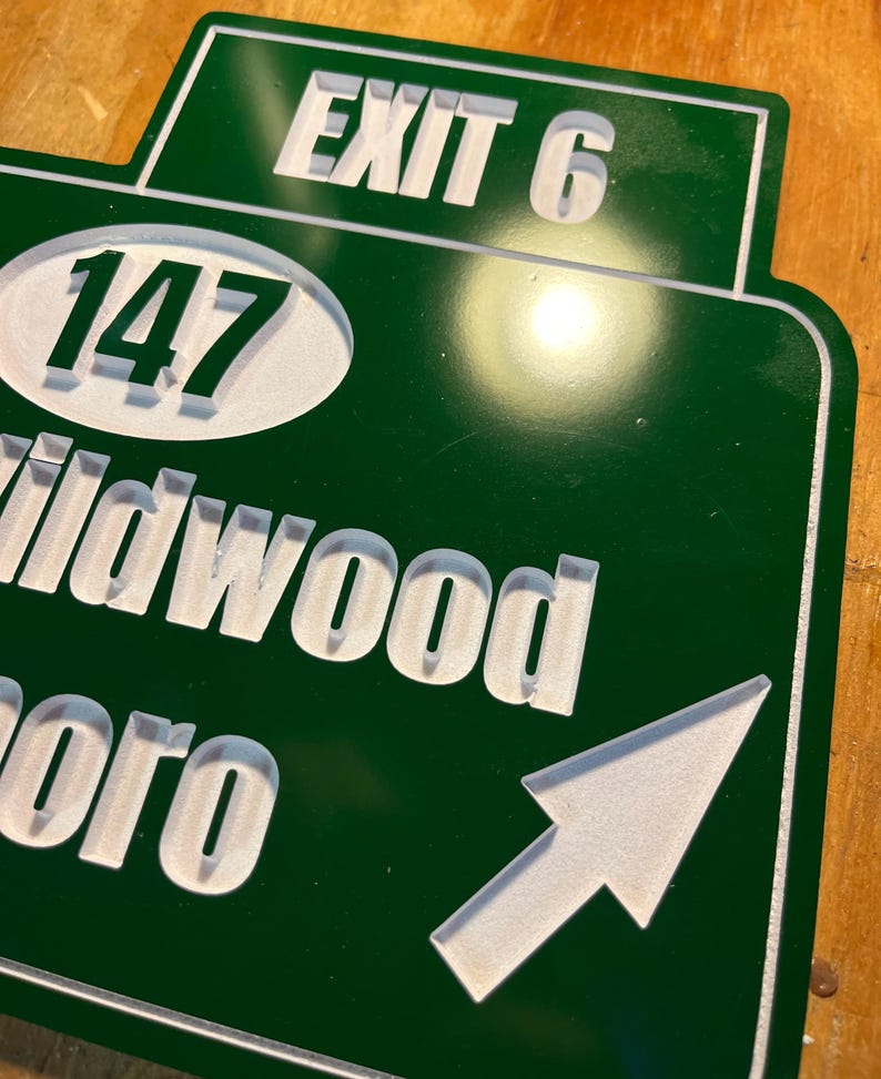 May include: A green and white road sign with the text "EXIT 6" at the top. Below, the number "147" is in a white oval. The sign also includes the words "Wildwood" and "boro" with a white arrow pointing right.