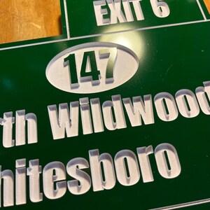 May include: A green and white road sign with the text "EXIT 6" at the top. Below, a white oval contains the number "147". The words "th Wildwood" and "hitesboro" are also visible in white, indicating a location.