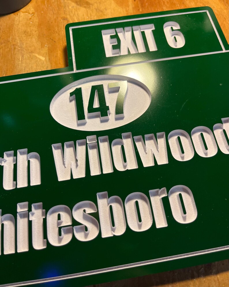 May include: A green and white road sign with the text "EXIT 6" at the top. Below, a white oval contains the number "147". The words "th Wildwood" and "hitesboro" are also visible in white, indicating a location.