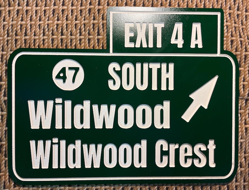 Puede incluir: Un letrero de carretera verde y blanco con el texto "EXIT 4 A" en la parte superior. Debajo, se lee "47 SOUTH Wildwood Wildwood Crest" con una flecha blanca que apunta hacia la derecha. El letrero es rectangular con un borde blanco.