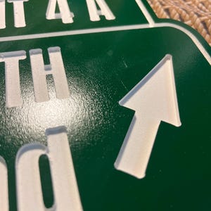 Puede incluir: Un letrero verde con letras blancas y una flecha blanca que apunta hacia arriba y hacia la derecha. El letrero dice "EXIT 4A", "TH" y "d". El letrero es probablemente para una autopista o carretera.