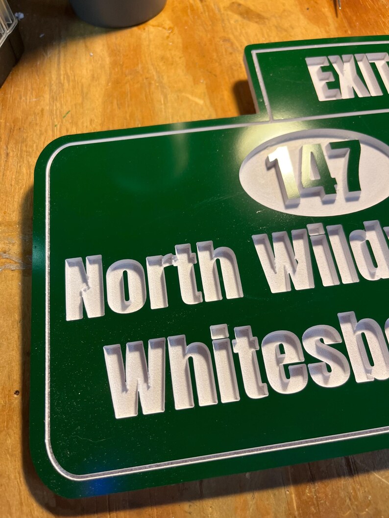 May include: A green and white road sign with the words "North Wilkesboro" and "Exit 147" in white lettering. The sign has a white border and is made of a glossy material.