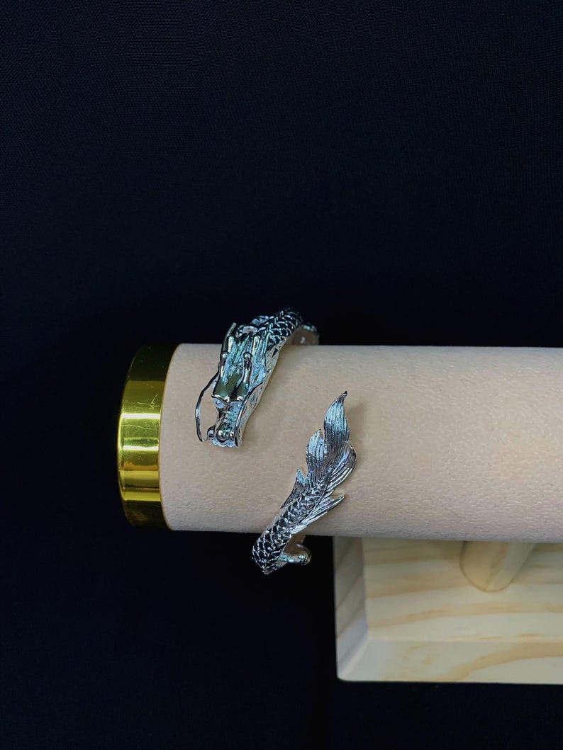 Close-up of a 925 sterling silver open cuff bracelet with two intricately detailed white dragon heads and a lustrous finish. The adjustable bangle flexes for a secure fit, blending mythical elegance with bridal-ready style.