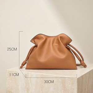 May include: A tan leather handbag with a drawstring closure. The bag is 11cm wide, 25cm tall, and 30cm long. The bag has a soft, gathered design and knotted drawstring handles.