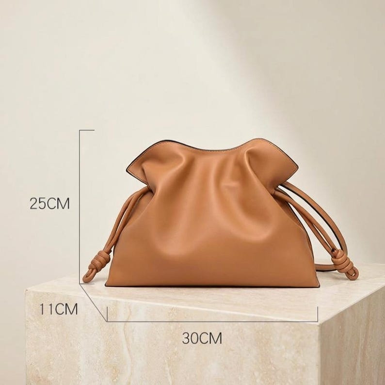 May include: A tan leather handbag with a drawstring closure. The bag is 11cm wide, 25cm tall, and 30cm long. The bag has a soft, gathered design and knotted drawstring handles.