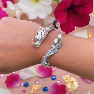Close-up of a 925 sterling silver open cuff bracelet with two intricately detailed white dragon heads and a lustrous finish. The adjustable bangle flexes for a secure fit, blending mythical elegance with bridal-ready style.
