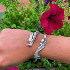 Close-up of a 925 sterling silver open cuff bracelet with two intricately detailed white dragon heads and a lustrous finish. The adjustable bangle flexes for a secure fit, blending mythical elegance with bridal-ready style.