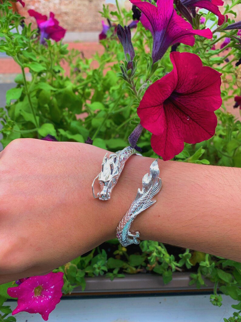 Close-up of a 925 sterling silver open cuff bracelet with two intricately detailed white dragon heads and a lustrous finish. The adjustable bangle flexes for a secure fit, blending mythical elegance with bridal-ready style.