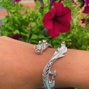 Close-up of a 925 sterling silver open cuff bracelet with two intricately detailed white dragon heads and a lustrous finish. The adjustable bangle flexes for a secure fit, blending mythical elegance with bridal-ready style.