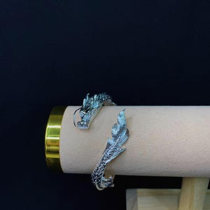 Close-up of a 925 sterling silver open cuff bracelet with two intricately detailed white dragon heads and a lustrous finish. The adjustable bangle flexes for a secure fit, blending mythical elegance with bridal-ready style.