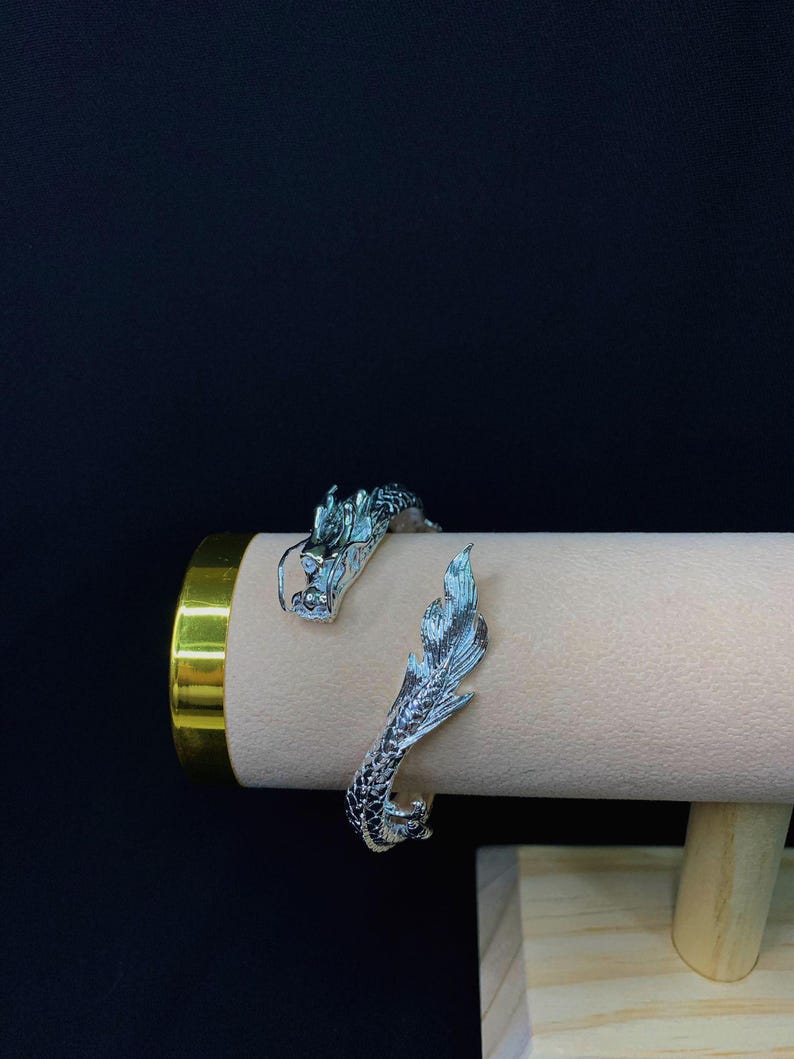 Close-up of a 925 sterling silver open cuff bracelet with two intricately detailed white dragon heads and a lustrous finish. The adjustable bangle flexes for a secure fit, blending mythical elegance with bridal-ready style.
