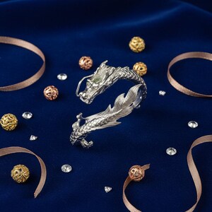 Close-up of a 925 sterling silver open cuff bracelet with two intricately detailed white dragon heads and a lustrous finish. The adjustable bangle flexes for a secure fit, blending mythical elegance with bridal-ready style.