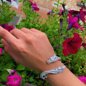 Close-up of a 925 sterling silver open cuff bracelet with two intricately detailed white dragon heads and a lustrous finish. The adjustable bangle flexes for a secure fit, blending mythical elegance with bridal-ready style.