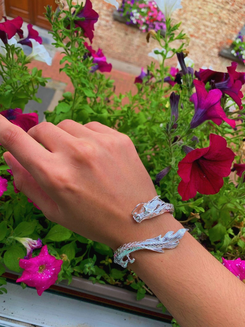 Close-up of a 925 sterling silver open cuff bracelet with two intricately detailed white dragon heads and a lustrous finish. The adjustable bangle flexes for a secure fit, blending mythical elegance with bridal-ready style.