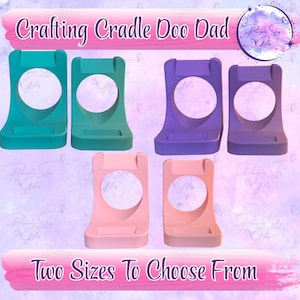 May include: Image of crafting cradles in teal, green, purple, and pink. Each cradle has a circular opening and a small shelf at the bottom. The text "Crafting Cradle Doo Dad" and "Two Sizes To Choose From" are displayed.