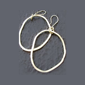 May include: A pair of gold-toned oval hoop earrings with a slightly irregular shape. The earrings are made of thin metal and have a simple, modern design.