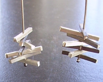 May include: A pair of silver earrings with a geometric design. Each earring features multiple stacked rectangular pieces of metal, creating a modern and abstract look.