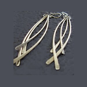 May include: A pair of long, silver dangle earrings with multiple strands of metal that are twisted and curved.