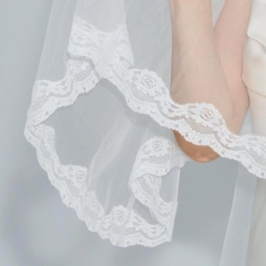 May include: White bridal veil with a delicate lace trim. The veil is made of soft tulle and is perfect for a wedding or special occasion.